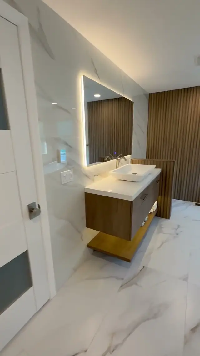 Primary bathroom in Burlington Township, NJ: a floating walnut-look vanity with a vessel sink under a backlit mirror, beside a fluted wood wall