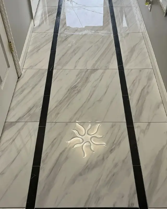 Large-format marble-look porcelain tile with a black border inlay