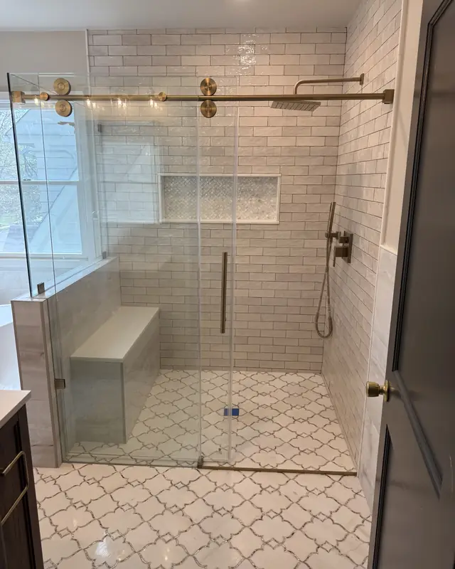 Walk-in shower with a brushed gold sliding glass door, built-in bench and arabesque tile floor