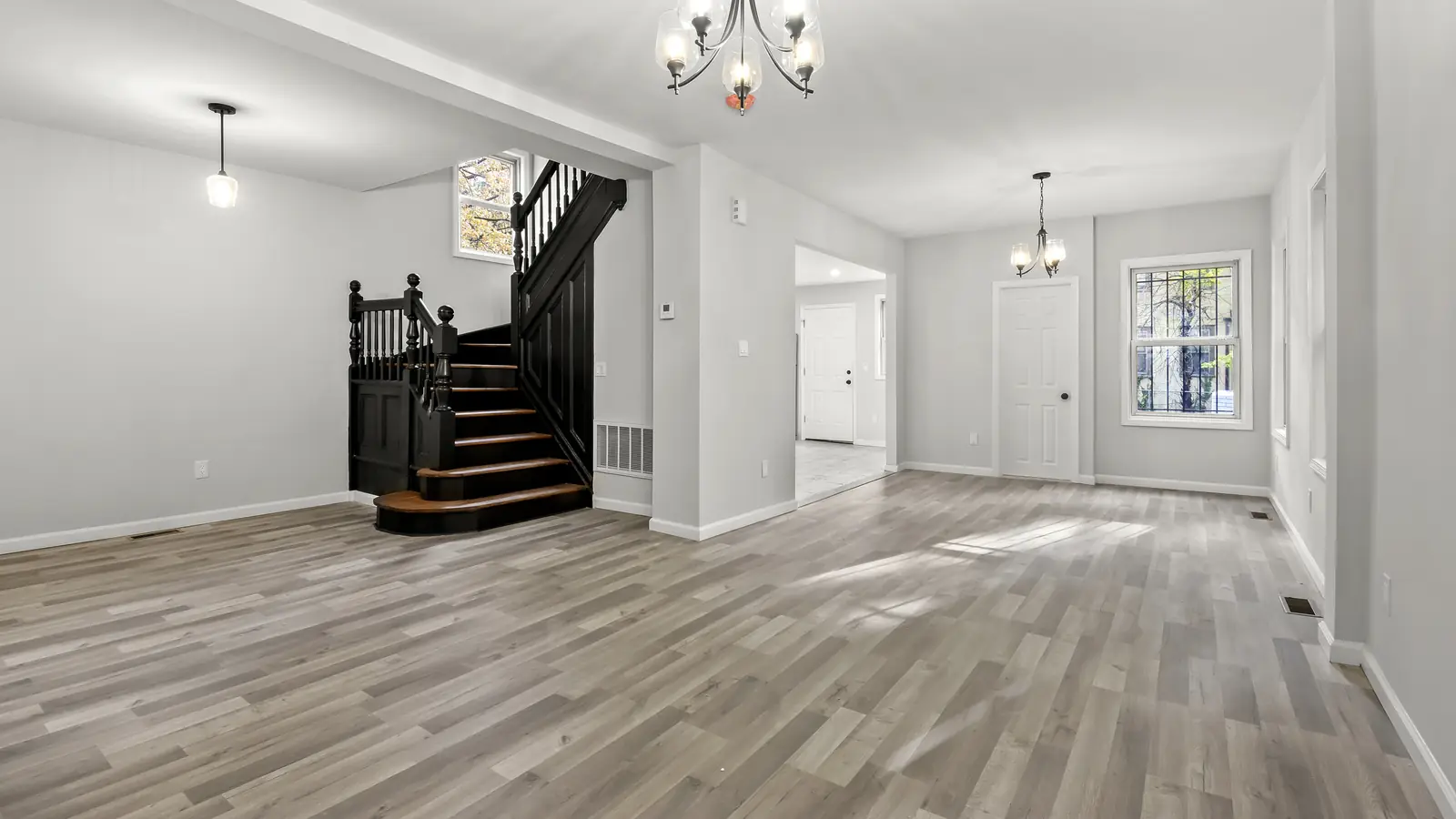Open first floor with new gray plank flooring, a dark wood staircase and fresh white trim