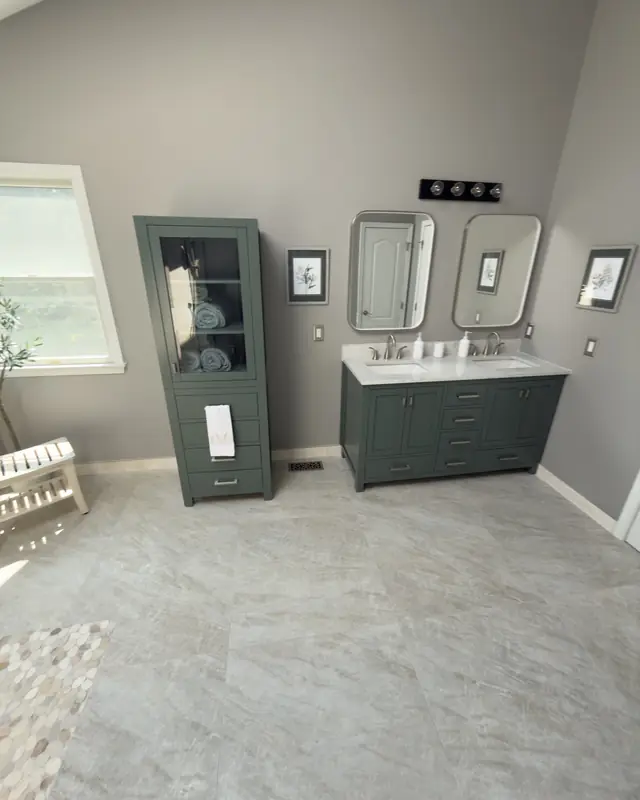 Green linen cabinet and double vanity by a window, with the pebble shower floor in the corner